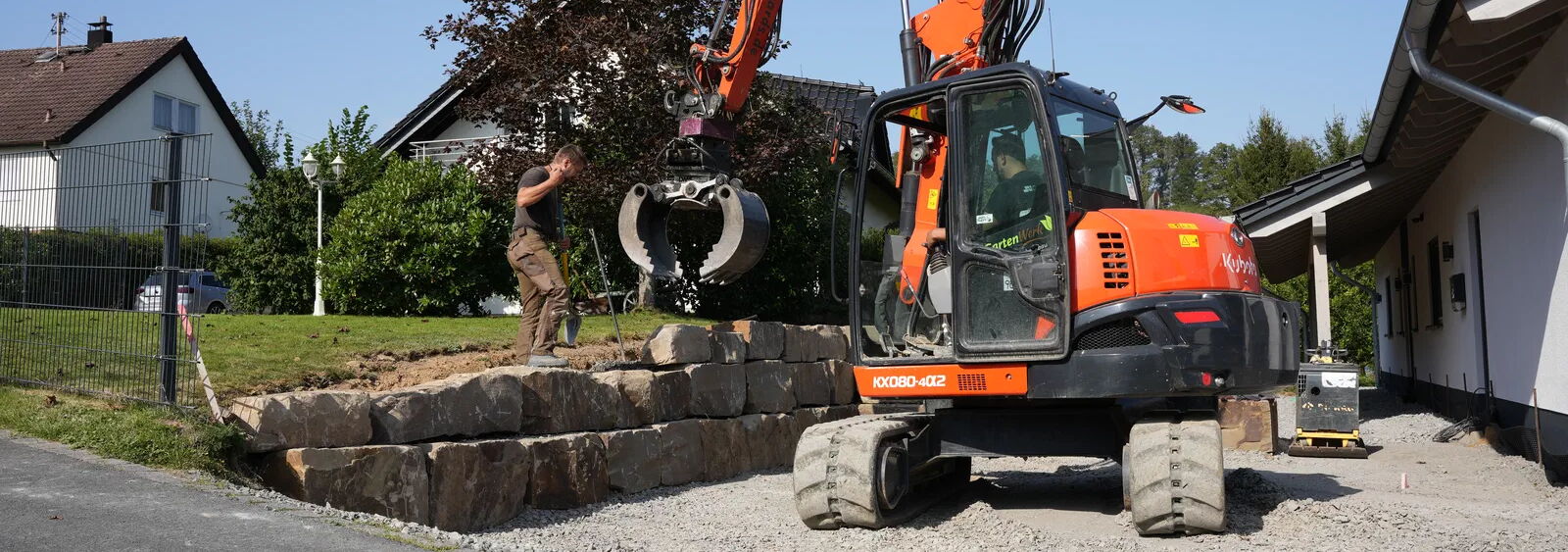 Verlegung von Findlingen mit Bagger und Greifzange in der Hauseinfahrt
