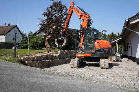 Verlegung von Findlingen mit Bagger und Greifzange in der Hauseinfahrt